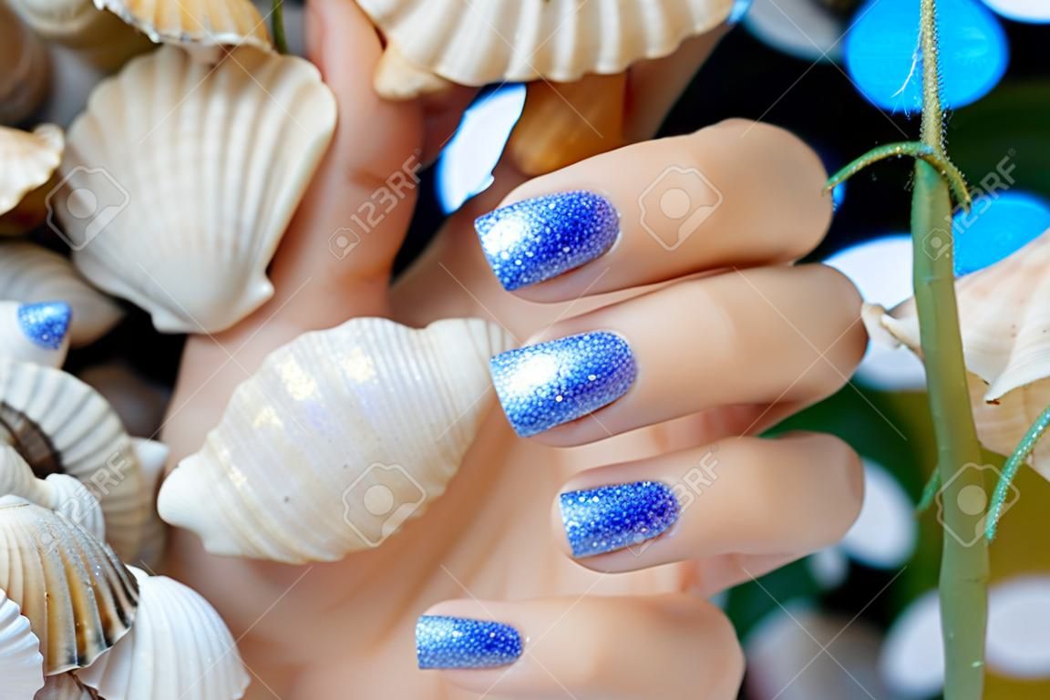 Sparkle beautiful blue manicure on a background of sea shells