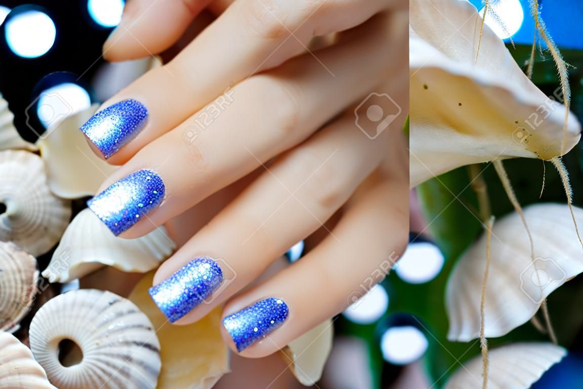 Sparkle beautiful blue manicure on a background of sea shells
