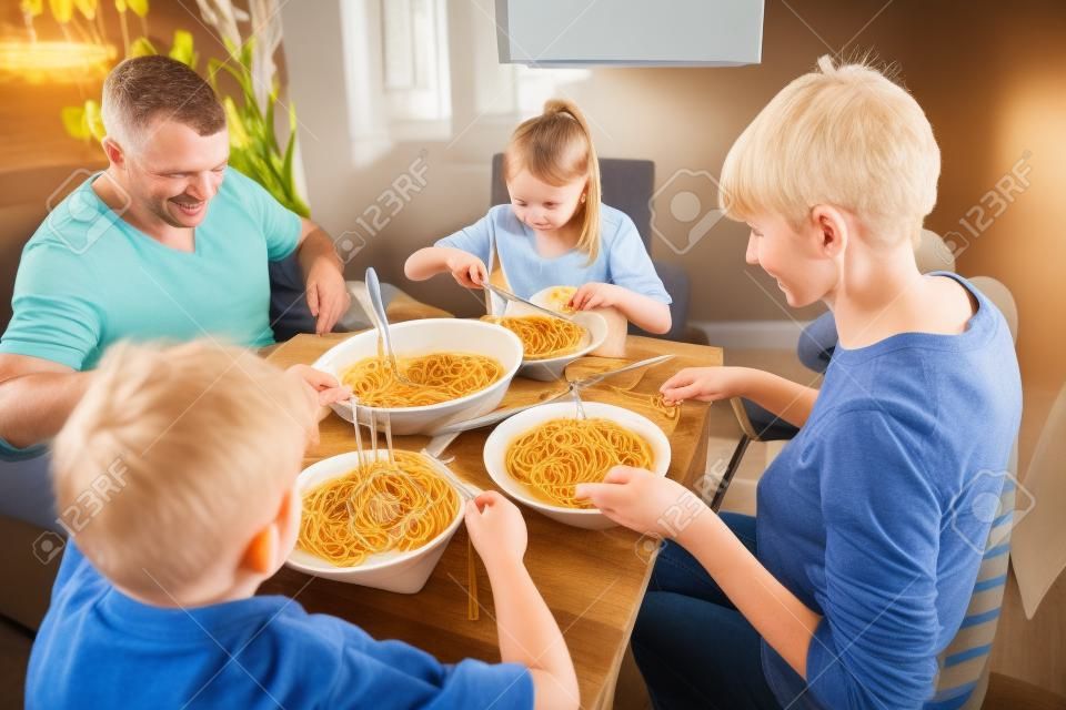 British family enjoying a spagetti bolognese together at home. They are sitting at the dining table with the baby girl in a baby seat. 