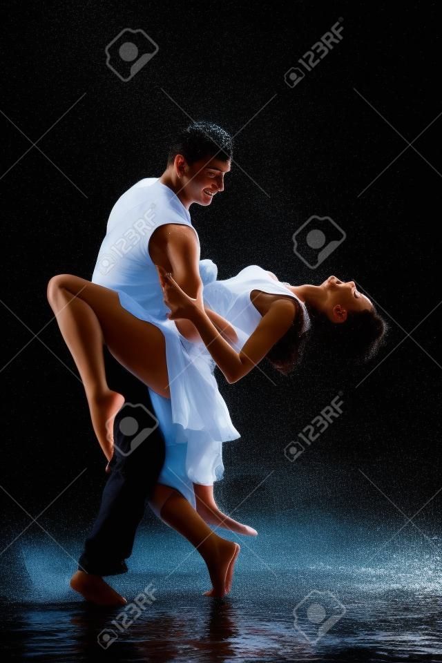 Young couple dancing in water under rain on a black background.  Modern dances.