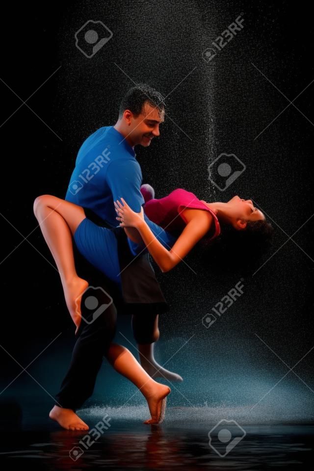 Young couple dancing in water under rain on a black background.  Modern dances.