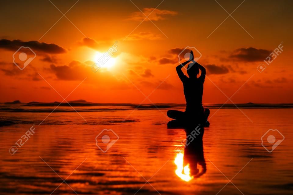 Silueta joven mujer practicando yoga en la playa al atardecer