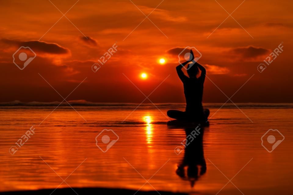 Silueta joven mujer practicando yoga en la playa al atardecer