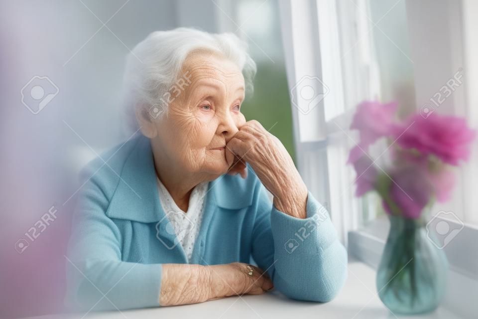 Elderly woman looks sadly out the window.