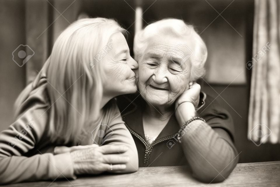 Ein kleines Mädchen küsst ihre glückliche Großmutter. Schwarzweißfoto.