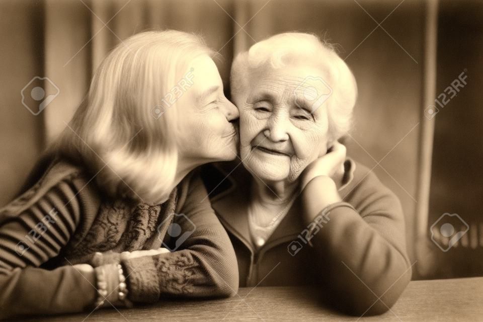Ein kleines Mädchen küsst ihre glückliche Großmutter. Schwarzweißfoto.