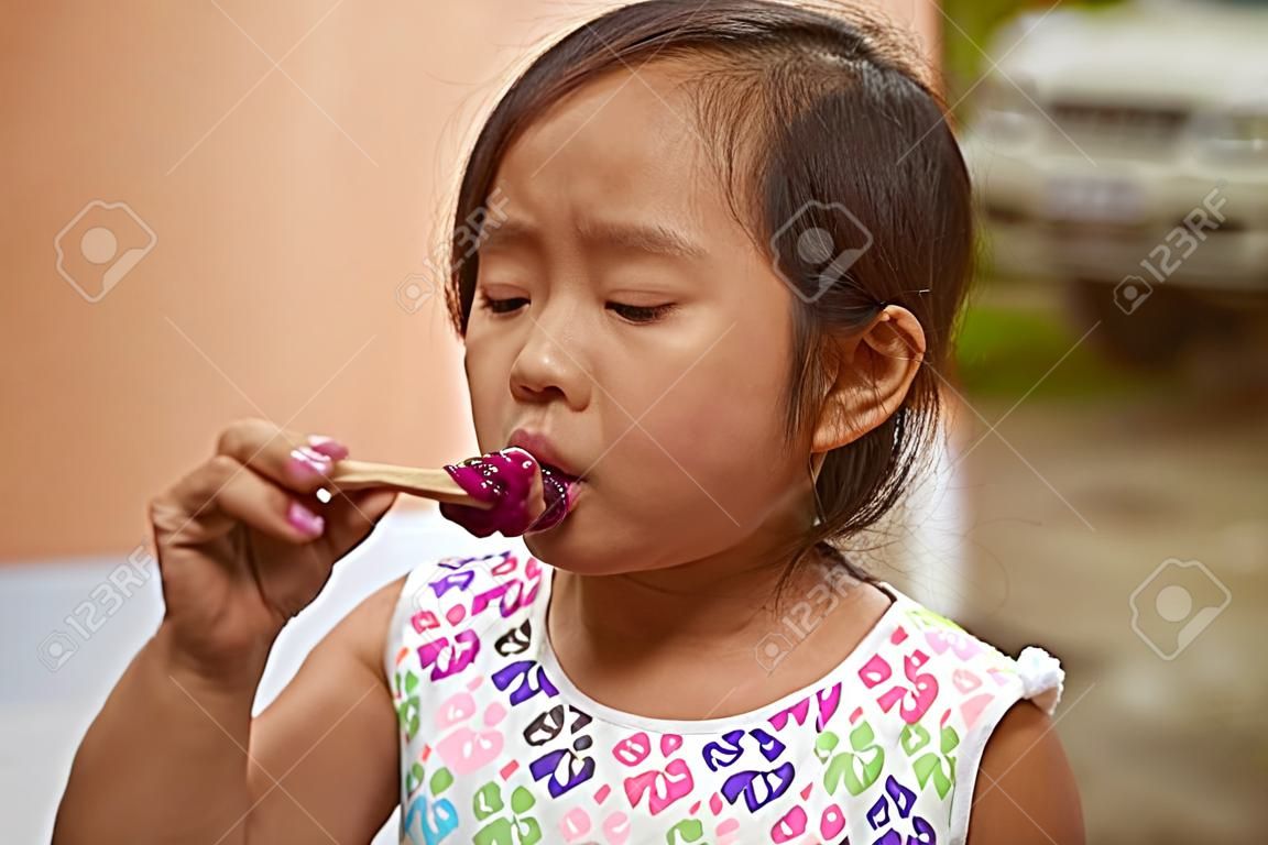 La piccola ragazza asiatica succhia il gelato sul bastone di legno