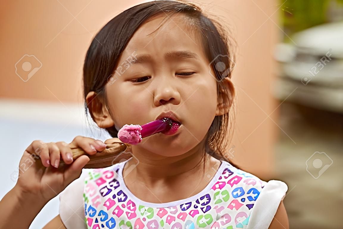 Small asian girl suck ice cream on wooden stick