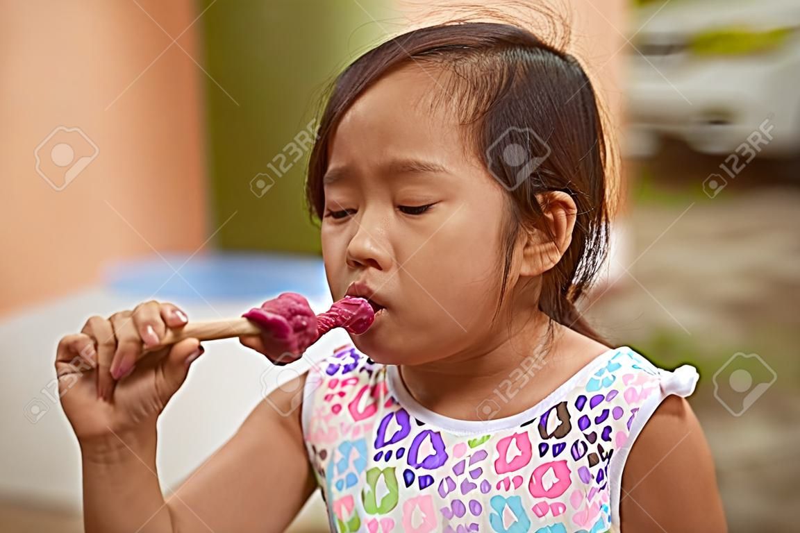 Pequena menina asiática chupar sorvete na vara de madeira