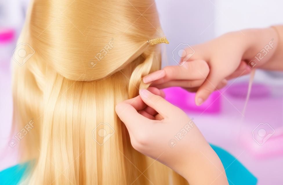The hairdresser does hair extensions to a young girl, a blonde in a beauty salon. Professional hair care.