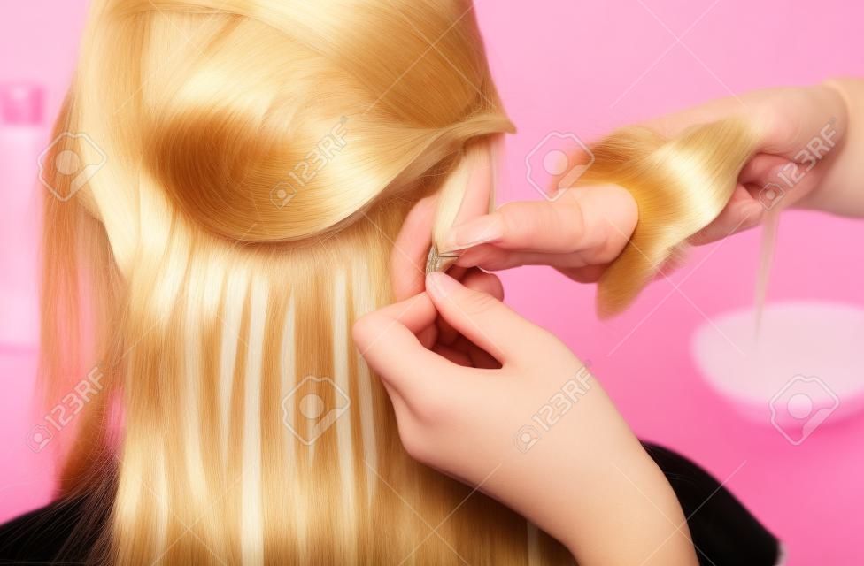 Der Friseur macht Haarverlängerungen für ein junges Mädchen, eine Blondine in einem Schönheitssalon. Professionelle Haarpflege.