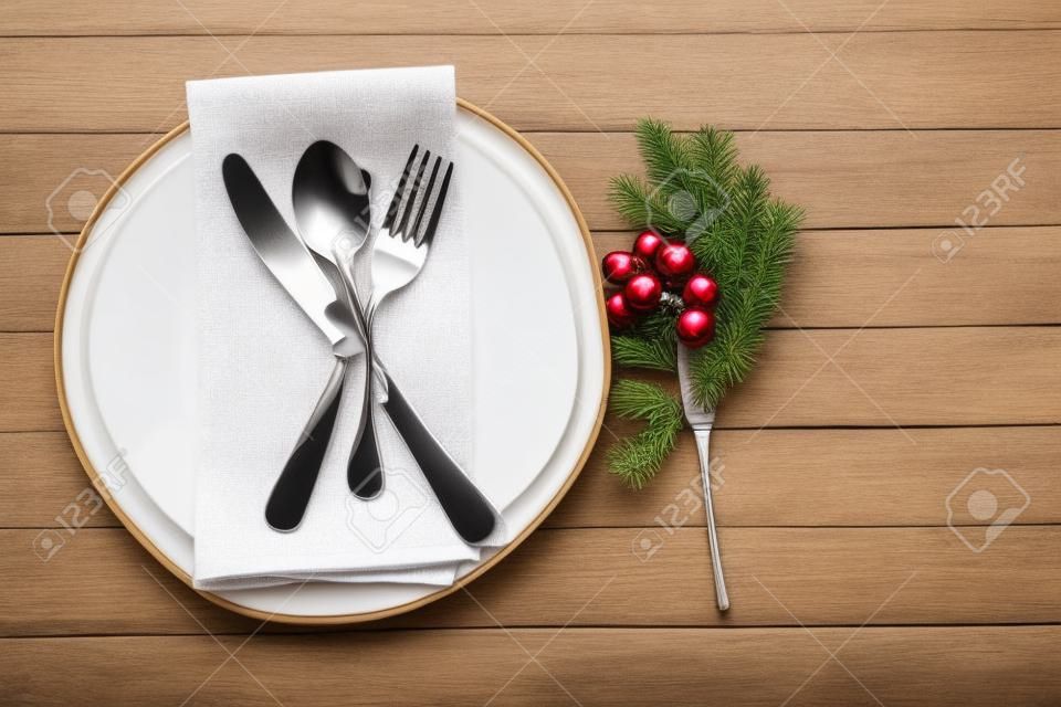 Vista aérea da configuração da mesa - um prato com colher, garfo e faca com uma decoração de Natal em um fundo de madeira.