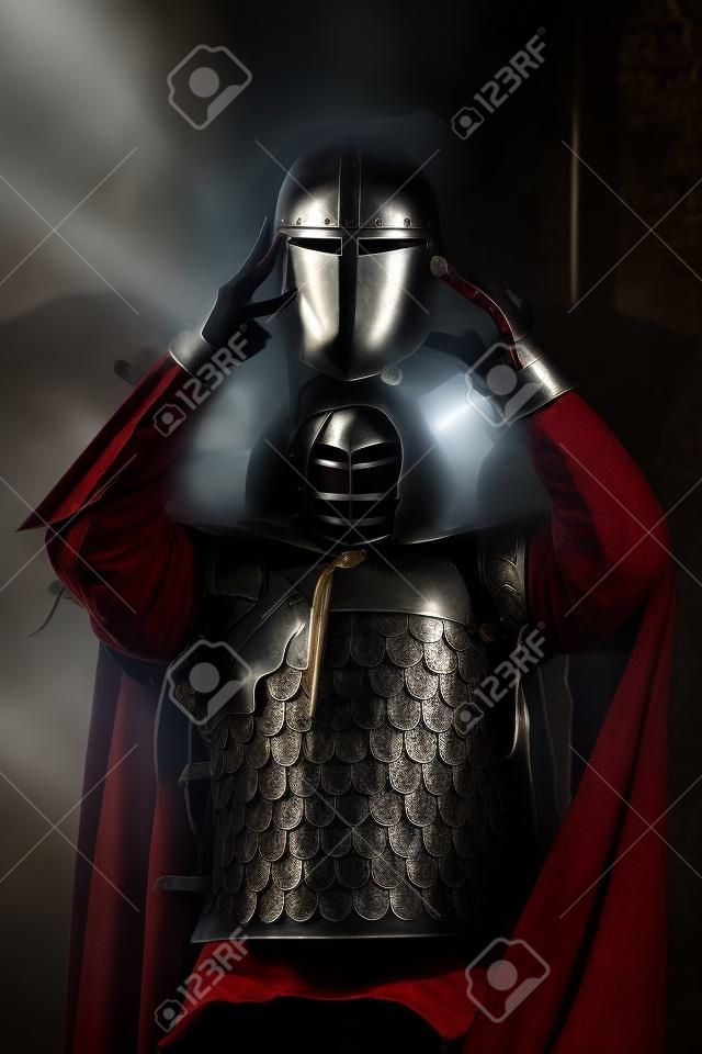 Medieval knight is going to wear a helmet. Portrait in the shadows.
