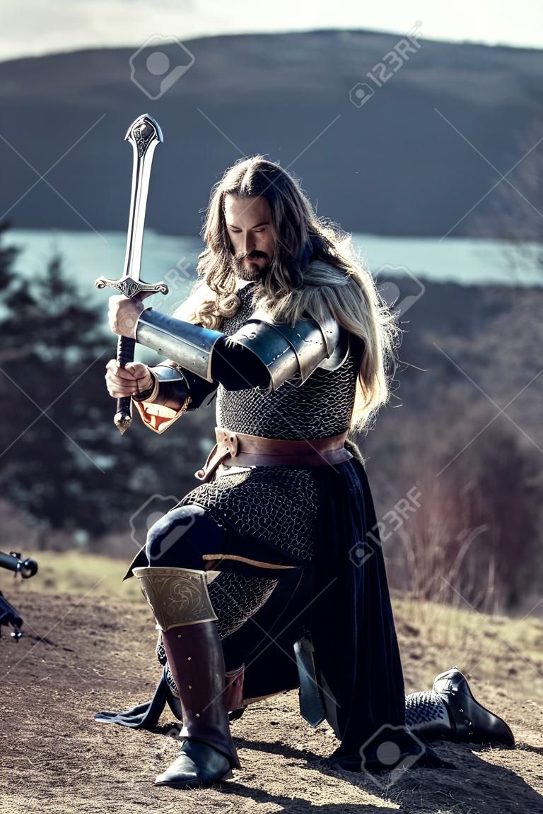 Long haired knight with the two-handed sword. Medieval rural background.
