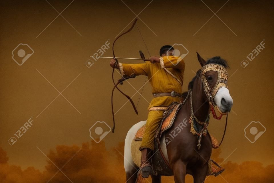 Mężczyzna w stroju etnicznym jedzie na koniu i celuje z łuku.