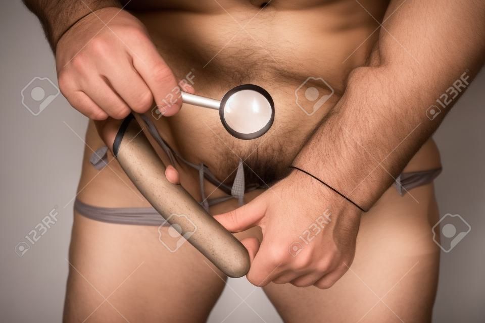 Being dissatisfied with the size of your penis or have psychological disorders that lead to impotence. Young handsome man holding a magnifying glass, hand pulls panties and looking at the penis.