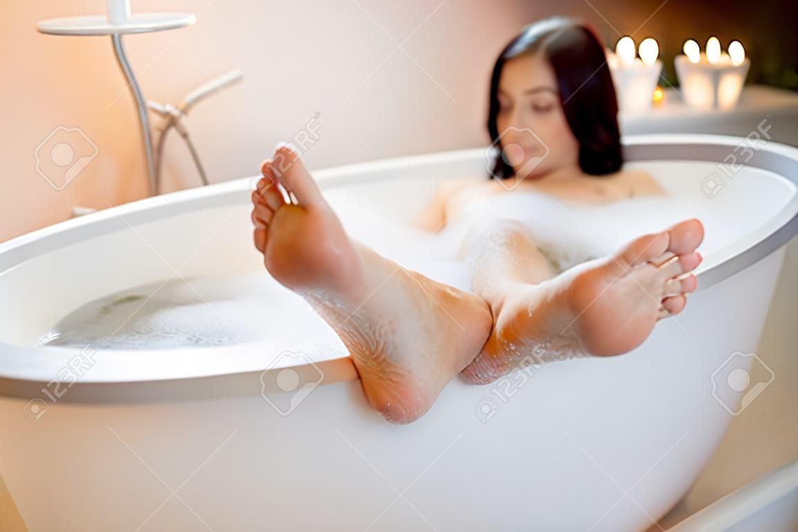 Junge Frau mit ihren Füßen auf dem Rand der Badewanne, die Badewanne