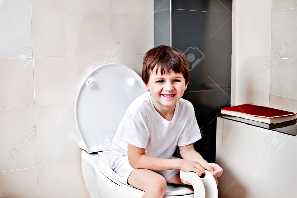 小7歲的男孩坐在馬桶。拿著白色衛生紙