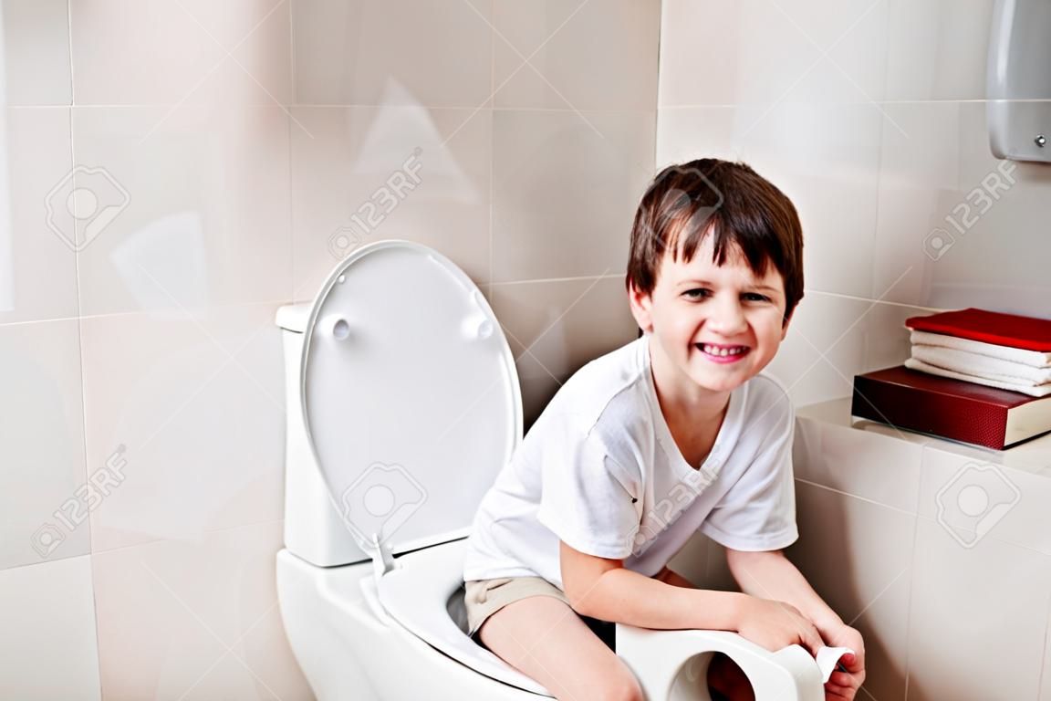 Kleine 7 jaar oude jongen zittend op het toilet.