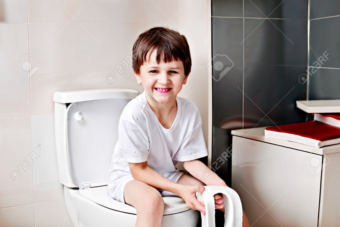 小7歲的男孩坐在馬桶。拿著白色衛生紙