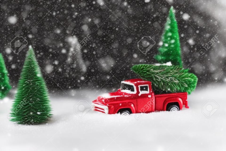 Red toy pickup car carrying Christmas tree in the snow