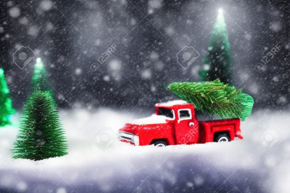 Red toy pickup car carrying Christmas tree in the snow