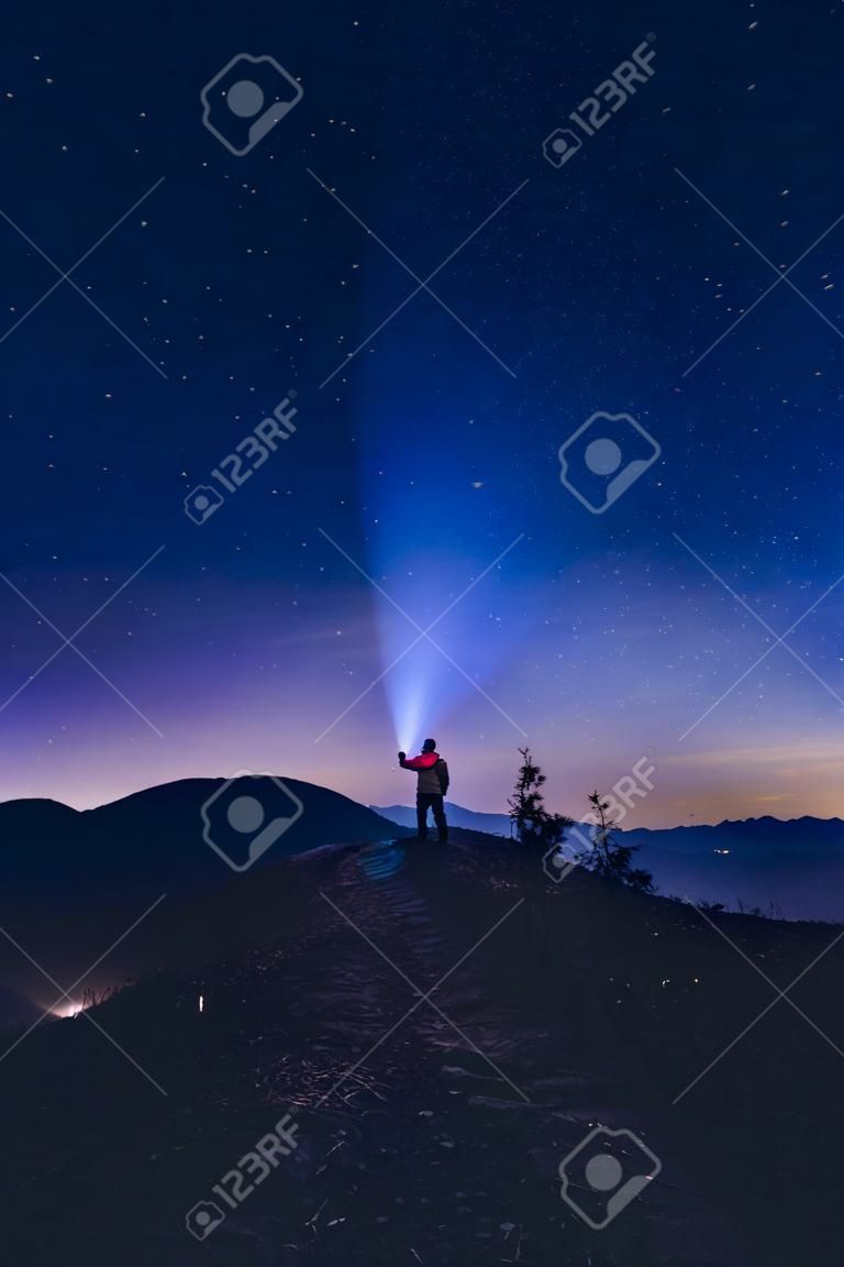 l & # 39 ; homme pointant la lumière de sa lampe de poche au coucher du soleil . camping dans la nuit. nuit de nuit