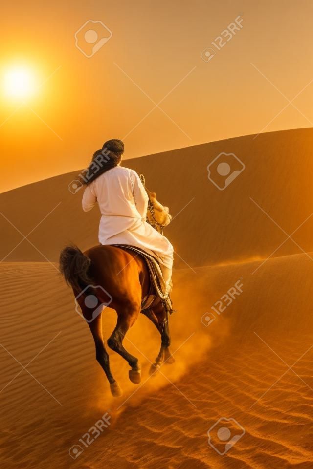 Un hombre de árabes anónimo en vestimenta tradicional, montando su caballo en la arena de un desierto bañado en oro de luz solar