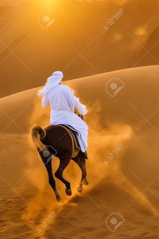 Un hombre de árabes anónimo en vestimenta tradicional, montando su caballo en la arena de un desierto bañado en oro de luz solar