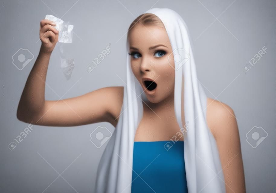 Surprised young woman holding condom on white background