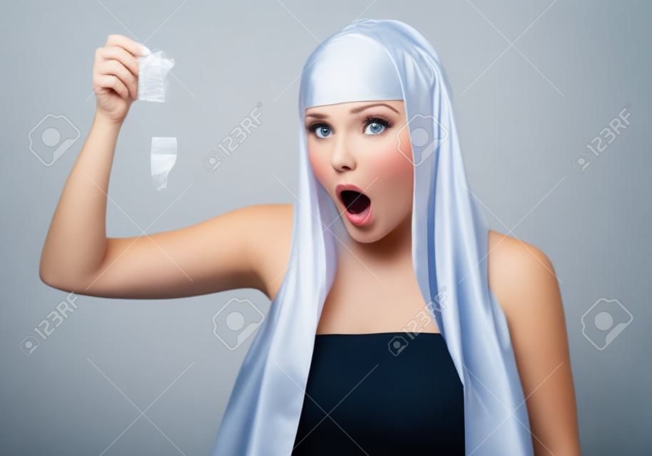 Surprised young woman holding condom on white background