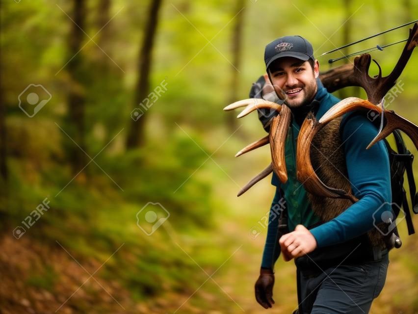 弓を持つハンターは森の中を歩き、背中にエルクや鹿の角を運びます。