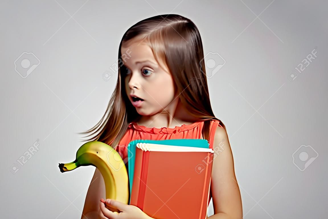 kleines Mädchen in einer Weste hält eine Banane.