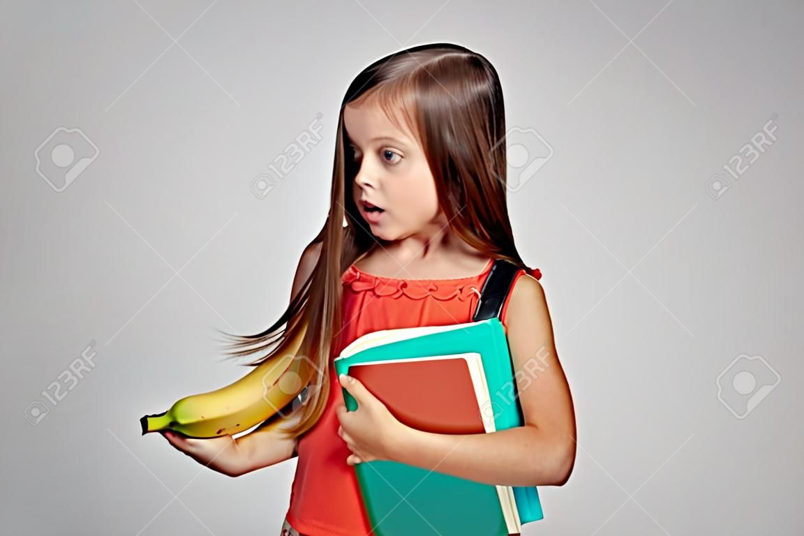 kleines Mädchen in einer Weste hält eine Banane.