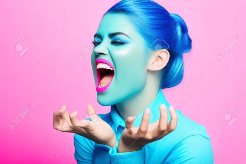 mujer enérgica con maquillaje brillante y en una camisa azul sobre un fondo rosa gestos con las manos