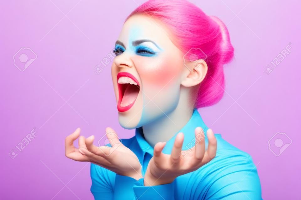 mujer enérgica con maquillaje brillante y en una camisa azul sobre un fondo rosa gestos con las manos