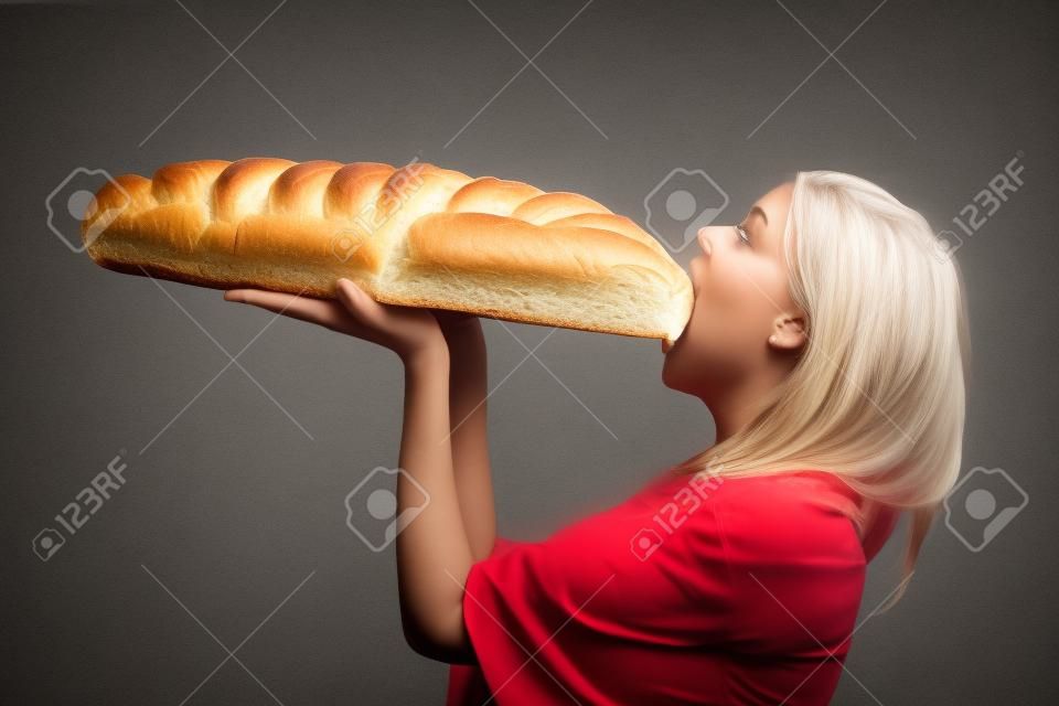 hungry woman eating large loaf of bread loaf side view light background