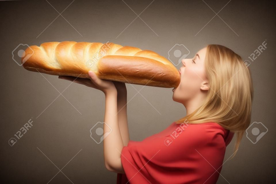 hungry woman eating large loaf of bread loaf side view light background