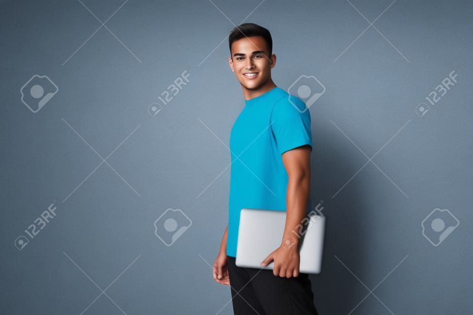 Jovem sério bronzeado bonito estudante homem na t-shirt básica segurar laptop pc posando isolado sobre fundo de estúdio branco. Copiar espaço Banner Mockup. Conceito de reparo de eletrônicos. Oferta de educação