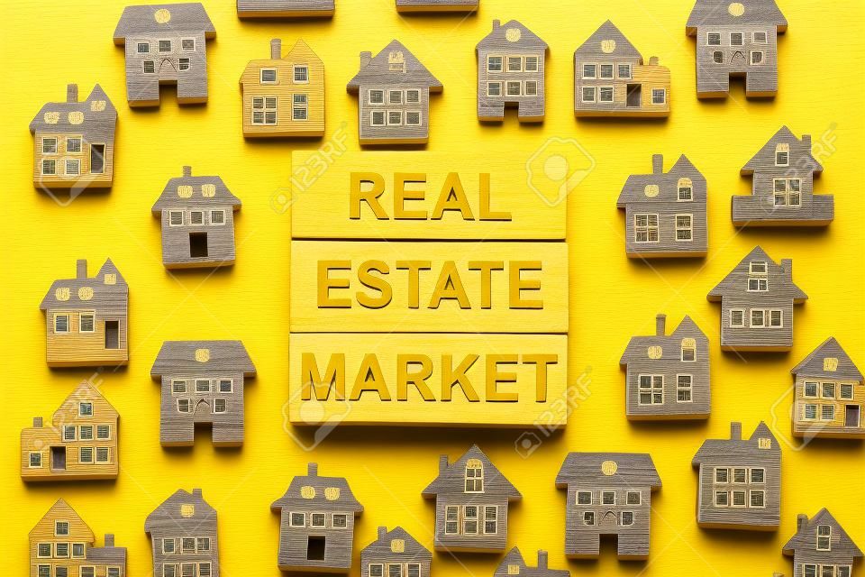 Des blocs de bois forment les mots «marché immobilier», des maisons en bois miniatures. Beau fond jaune, copiez l'espace. Notion d'entreprise.