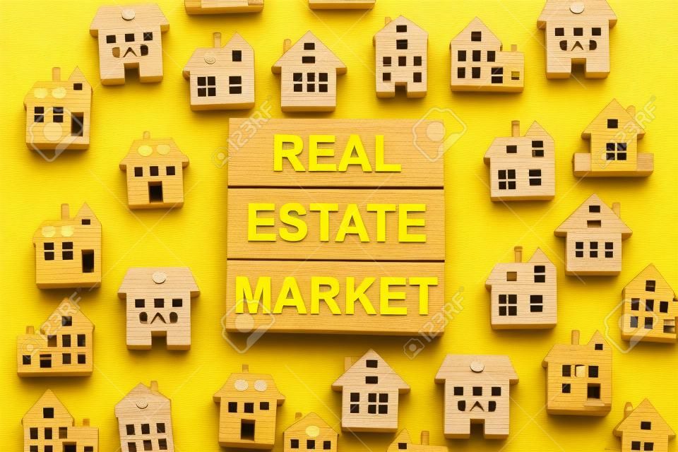Des blocs de bois forment les mots «marché immobilier», des maisons en bois miniatures. Beau fond jaune, copiez l'espace. Notion d'entreprise.