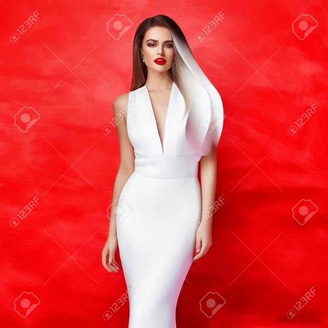 Молодая красивая женщина создает потрясающие длинные элегантный белый вечернее платье и красные туфли против стильный красном фоне