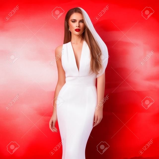 Jovem bela mulher deslumbrante posando em longo elegante vestido de noite branco e sapatos vermelhos contra elegante fundo vermelho