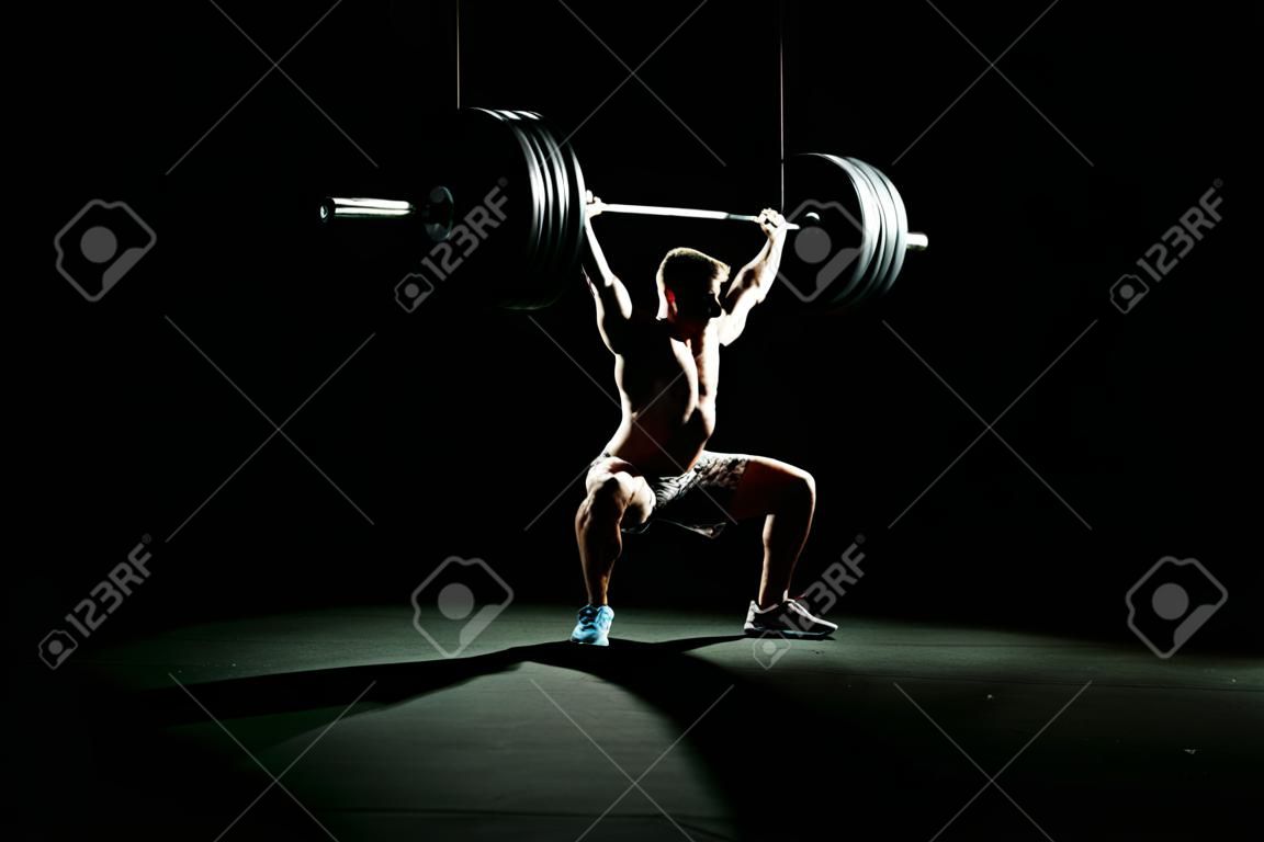 Fitness training. Man doing sit ups exercise with barbell in dark gym.