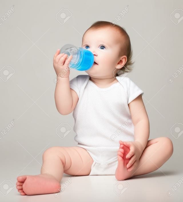 Infant child baby toddler sitting and drinking water from the feeding bottle on a white background