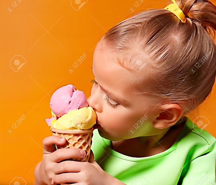 吃俏麗的女嬰的孩子在黃色背景的奶蛋烘餅錐體吃舔香蕉和草莓冰淇凌