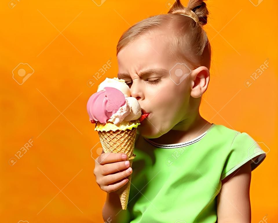 Pretty baby girl kid eating licking banana and strawberry ice cream in waffles cone on yellow background with free text copy space