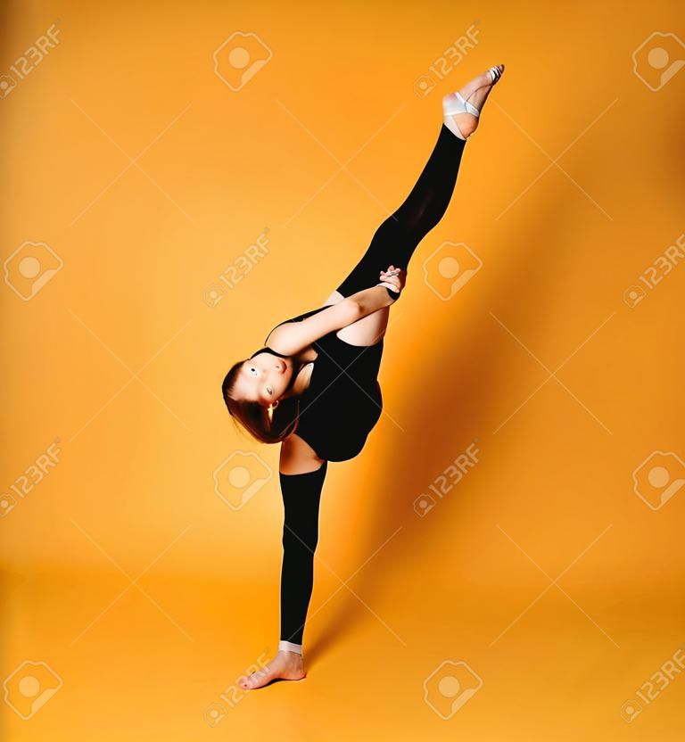 A ginasta rítmica flexível da menina adolescente no maiô e nas meias faz divisões verticais segurando sua perna acima com ambas as mãos sobre sua cabeça olhando para nós no fundo com espaço livre da cópia