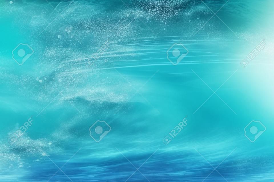 Foto subaquática de oceano onda extrema quebrando na praia tropical com spray, espuma, ondulações na superfície da água e padrão de bolhas. Fundo abstrato de cor azul claro do mar claro surf com textura