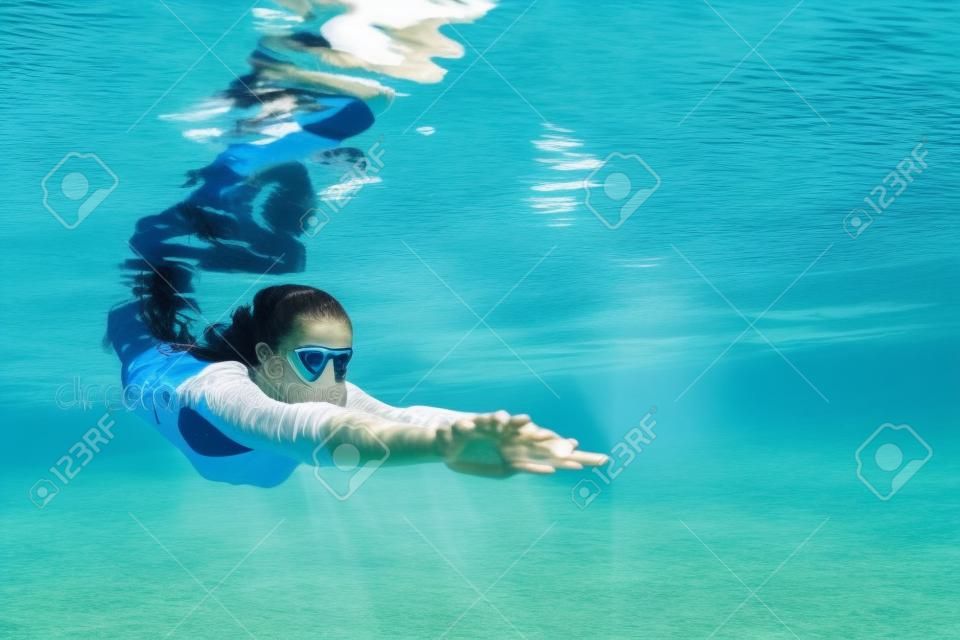 Giovane e bella donna subacquea immersioni con divertimento da bordo vasca alla piscina blu. Sano stile di vita attivo, attività sportiva gente acqua per mantenere in forma e lezioni di nuoto in centro benessere in vacanze estive.